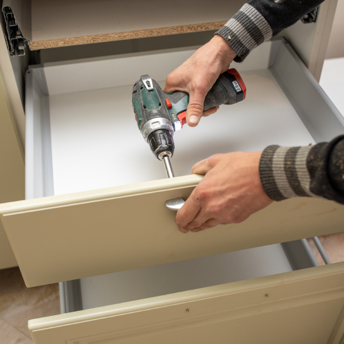 Technician installs white oak cabinets in a new home in Woodland Hills, CA using a drill.<br />
