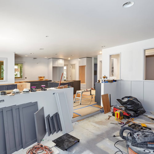 Painted cabinet doors, shelves, tools, lights, and trash bags in kitchen and family room during a kitchen remodel.